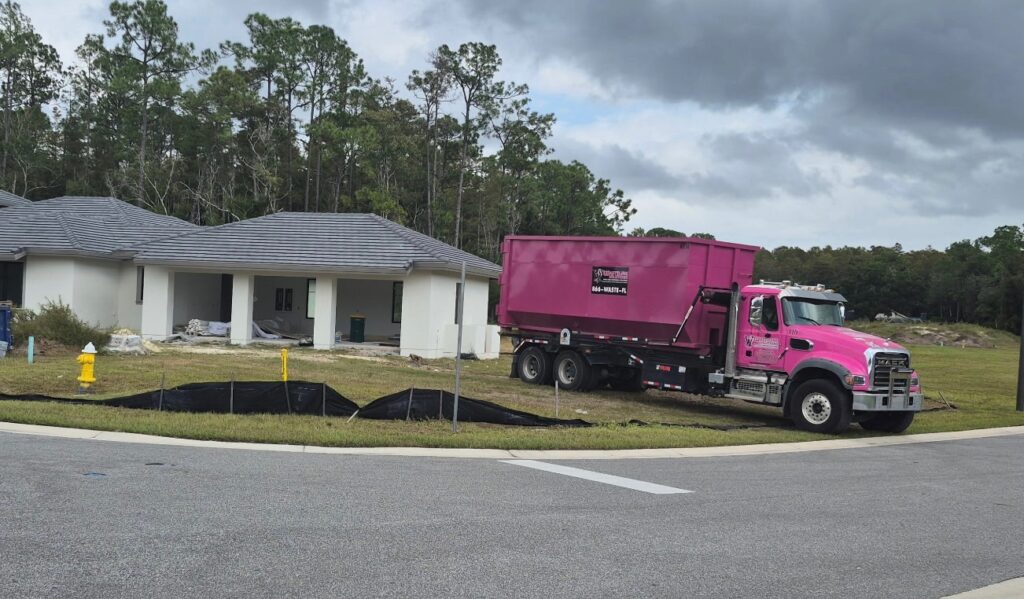 Wasteline Solutions pink dumpster truck at residential property for junk removal job
